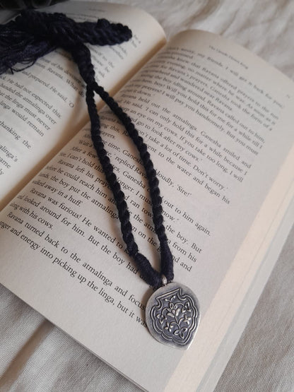 92.5 silver inverted oval pendant with Mughal pietra dura-inspired floral embossing. Black dori with tassels. Minimalist, heritage-inspired, daily wear. Shop Sadabahaar Jewelry.