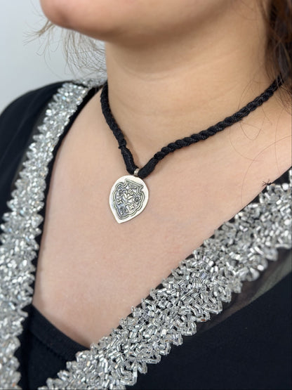 92.5 silver inverted oval pendant with Mughal pietra dura-inspired floral embossing. Black dori with tassels. Minimalist, heritage-inspired, daily wear. Shop Sadabahaar Jewelry.