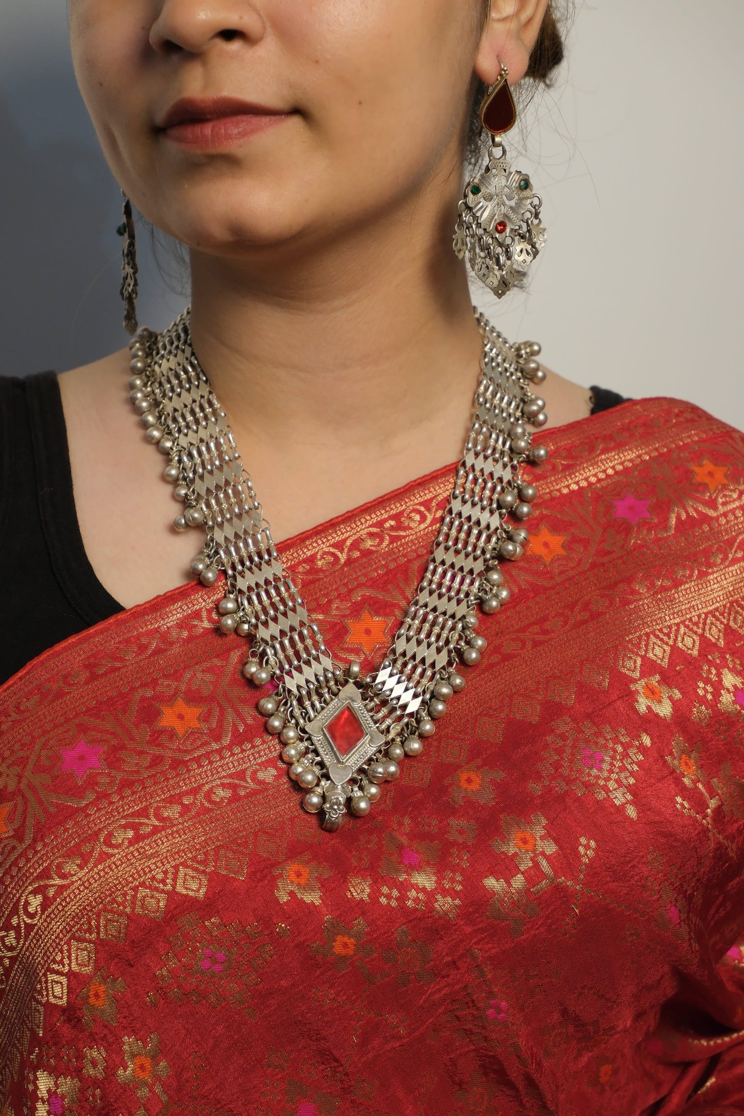 Close-up of a person wearing a red saree with intricate patterns and a silver necklace.