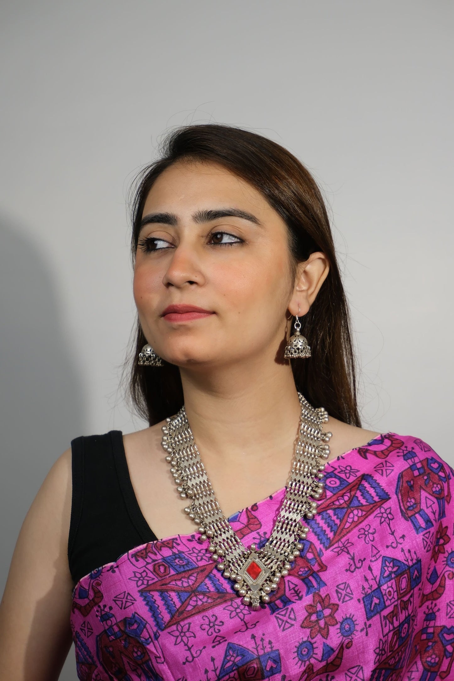 Woman wearing a pink traditional outfit with intricate patterns and jewelry on a plain background