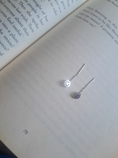 A pair of silver-toned dangle earrings with small circular charms, displayed on the pages of an open book.