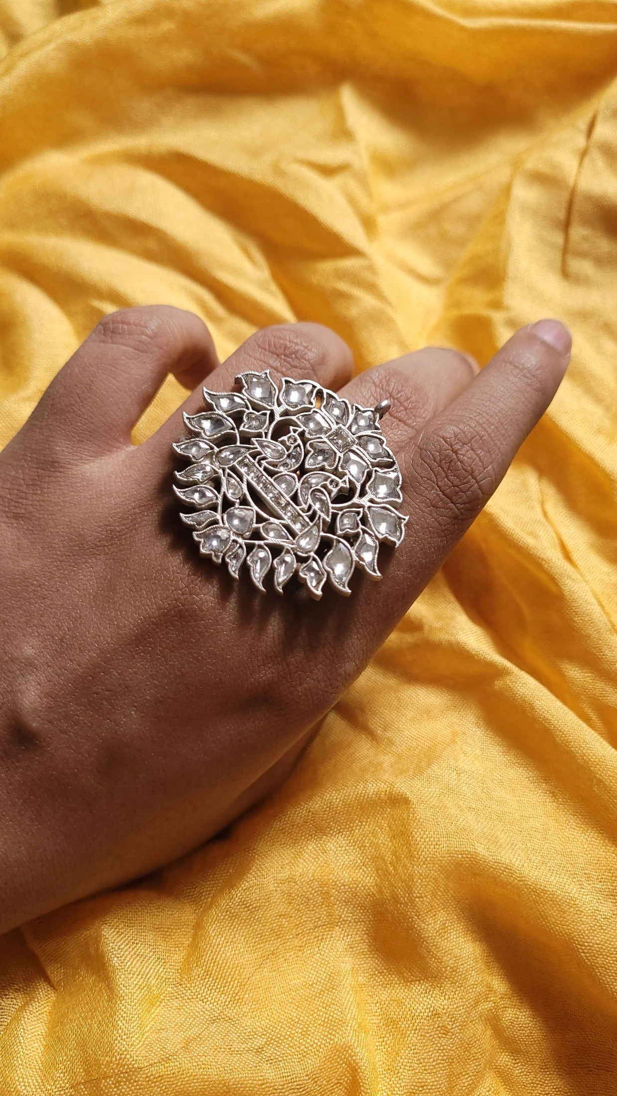 Silver ring with intricate design on a hand against a yellow fabric background
