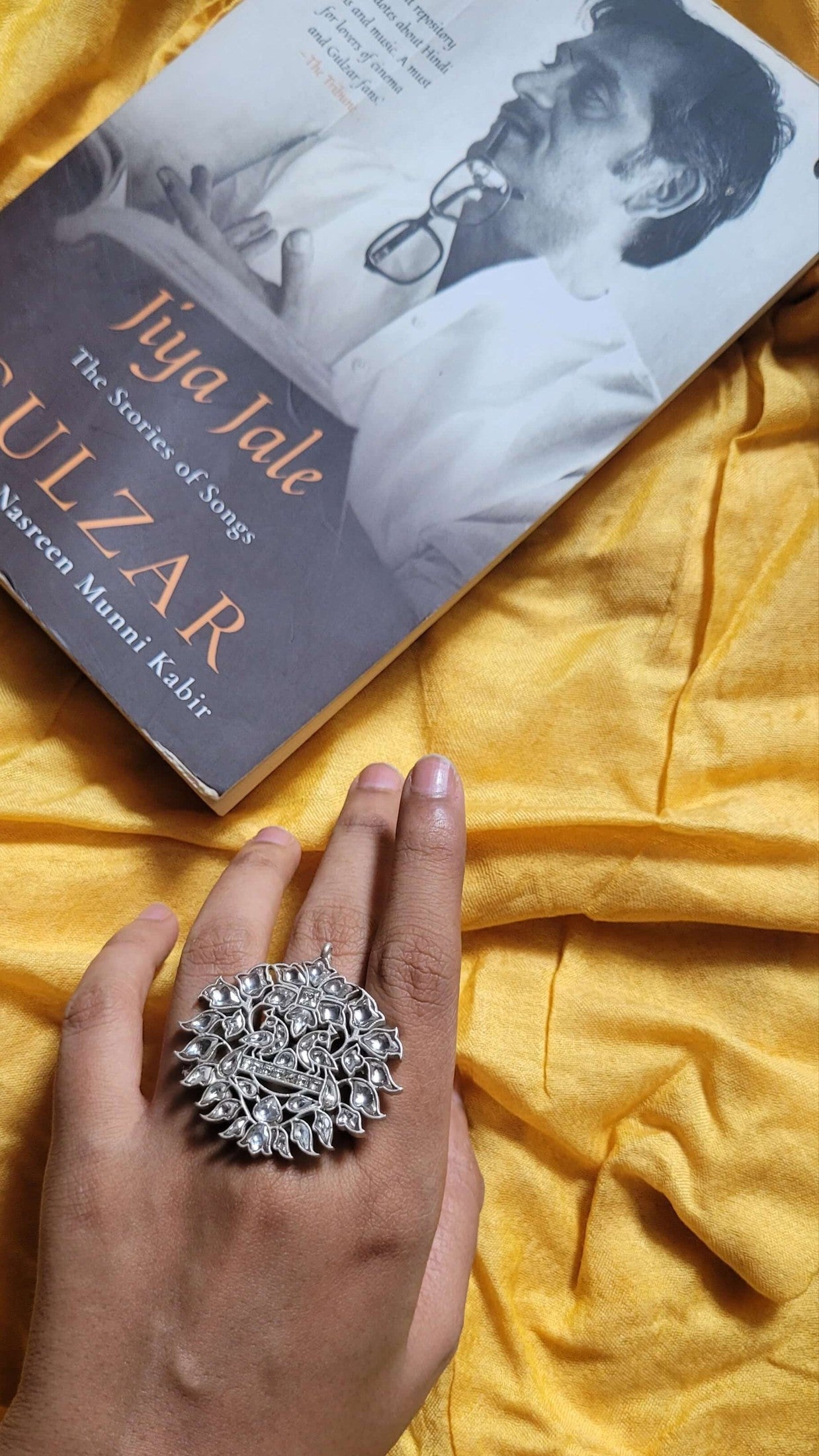 Book titled 'Gulzar' by Iqba Jalal on a yellow fabric background with a hand wearing Mythili Ring.