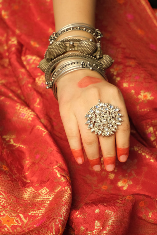 Hand with a silver ring and bangles on a red saree background