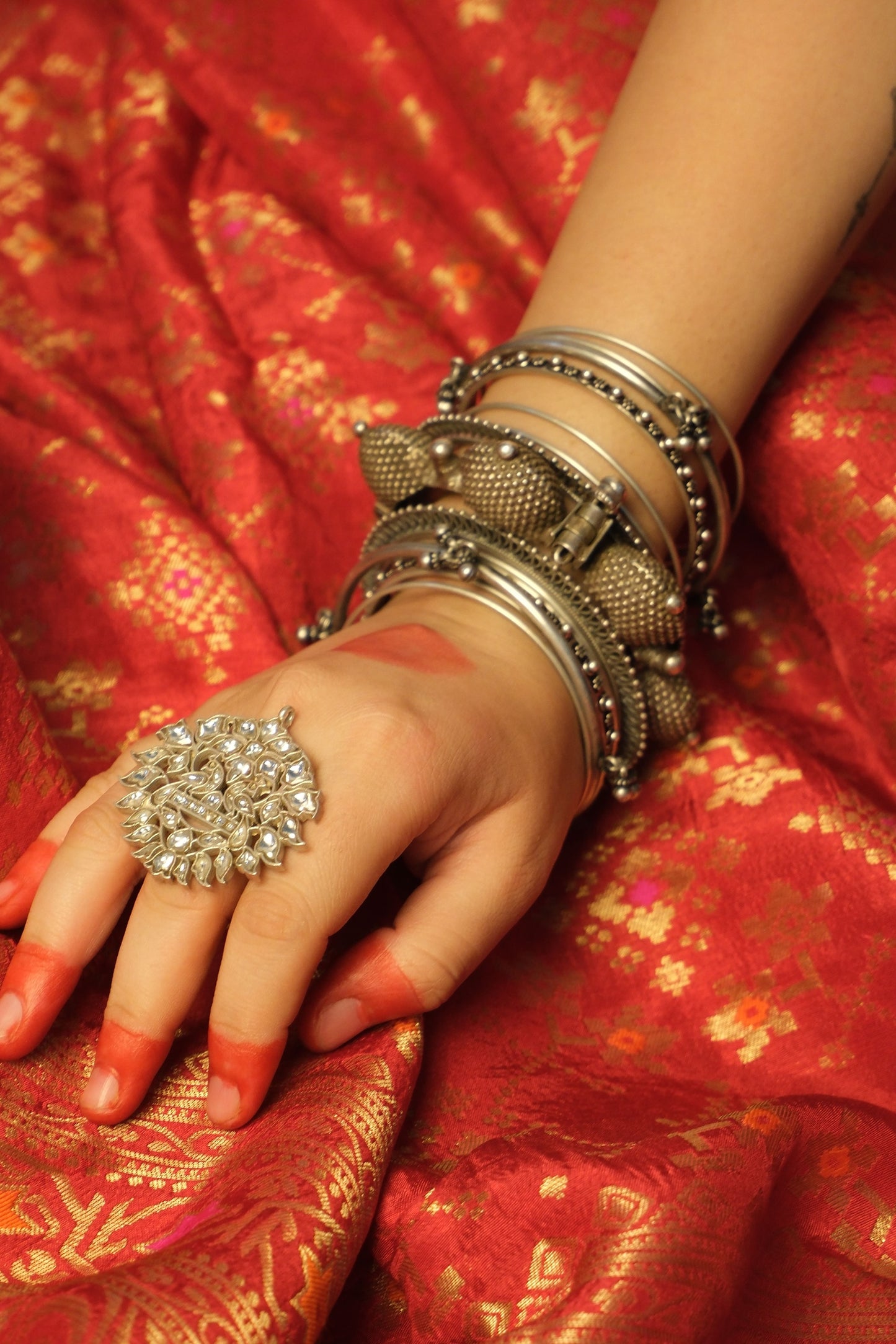 Hand wearing a silver ring and bangles on a red saree background