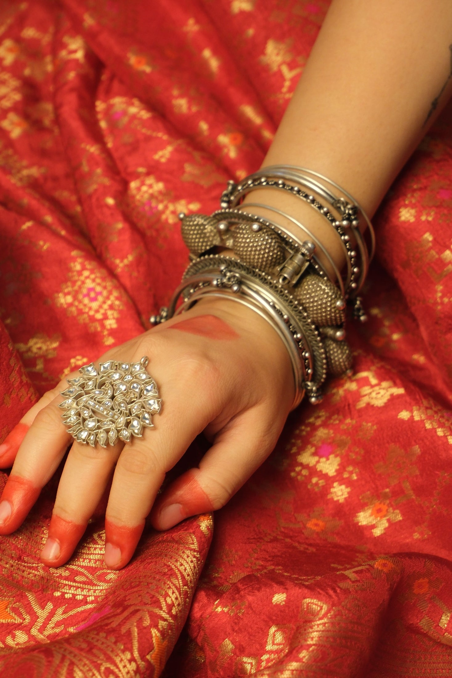 Hand wearing a silver ring and bangles on a red saree background