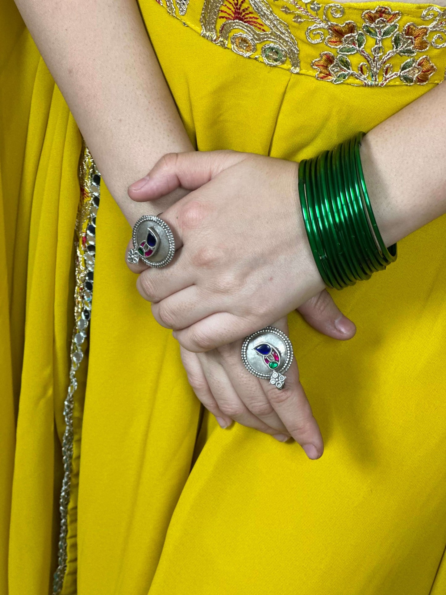 Close-up of hands wearing silver rings and green bangles against a yellow fabric background