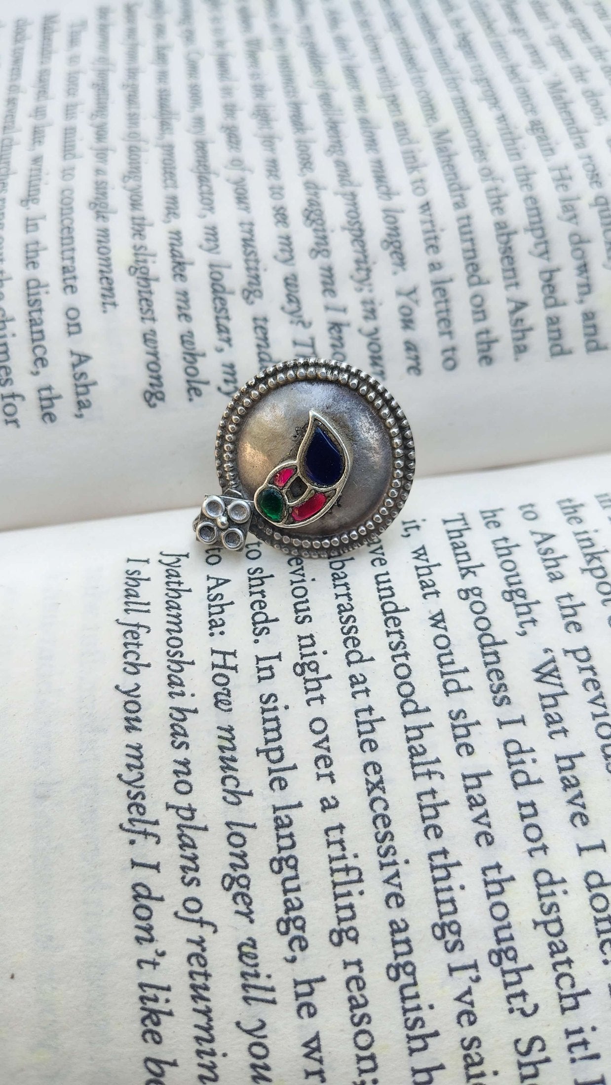 Vintage silver kundan ring with a red and blue stones on an open book