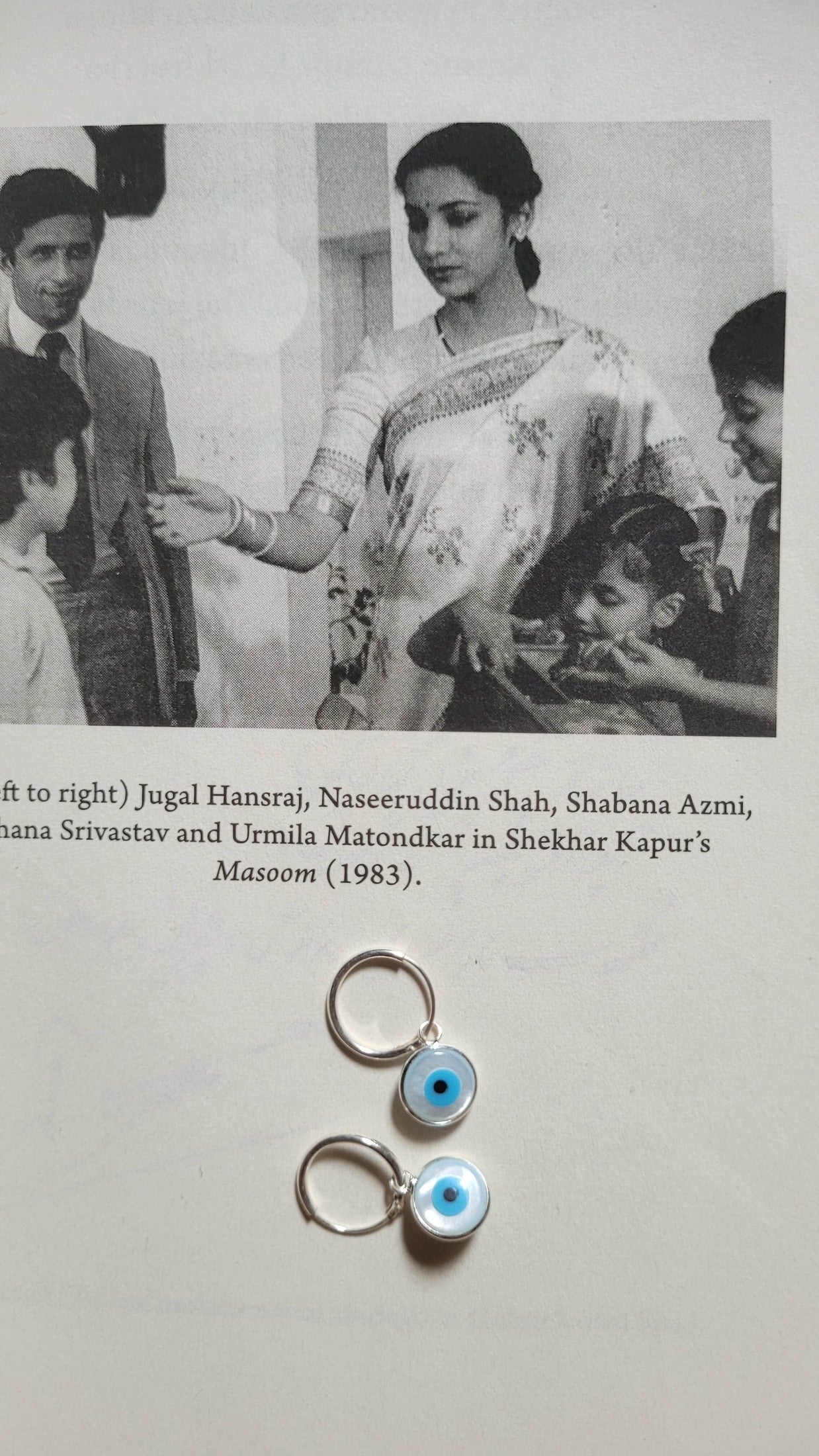 Black and white photo of a group of people with a pair of earrings featuring eye designs on a light gray background.