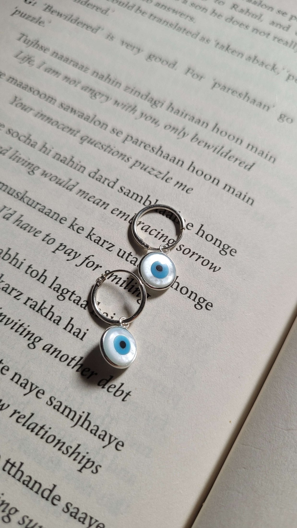 Two silver earrings with blue eye designs on an open book
