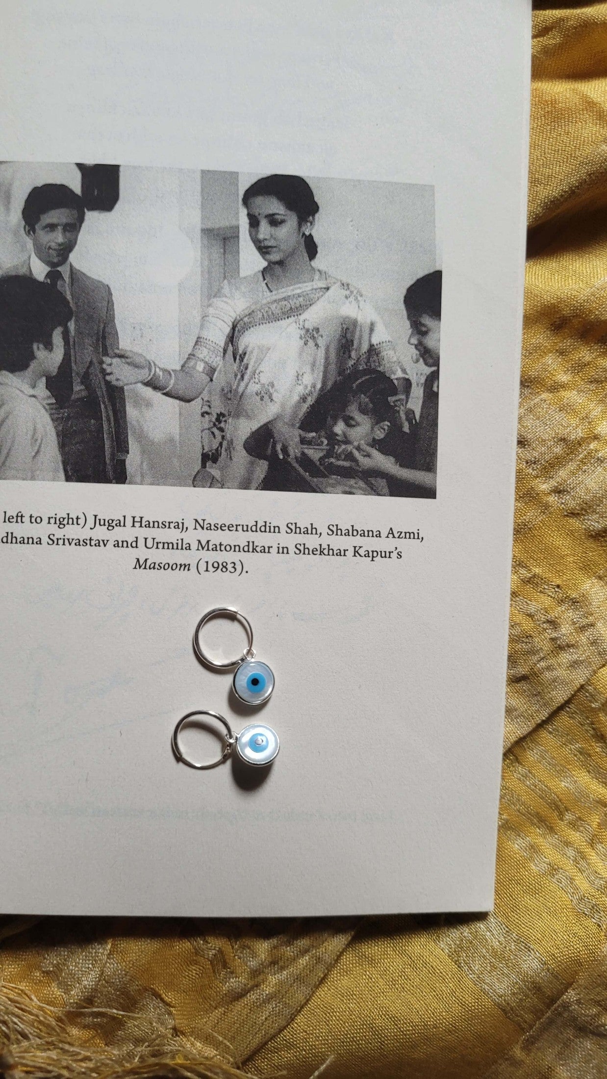 Vintage photo of a woman in a saree with text and hoops with an eye symbol on a yellow fabric background.