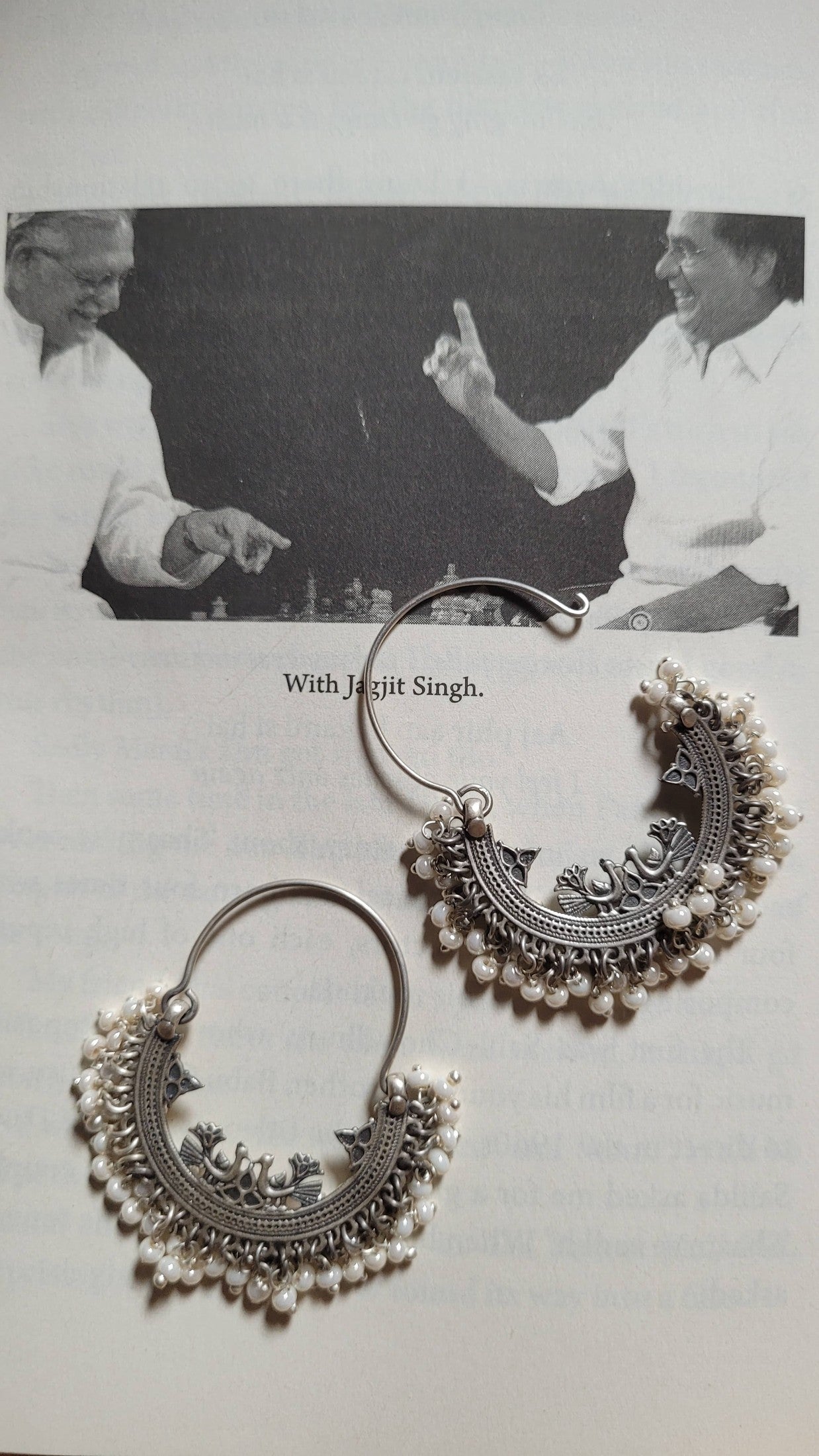 Ornate silver earrings on a light gray background with a black and white photo of two men  in the corner.