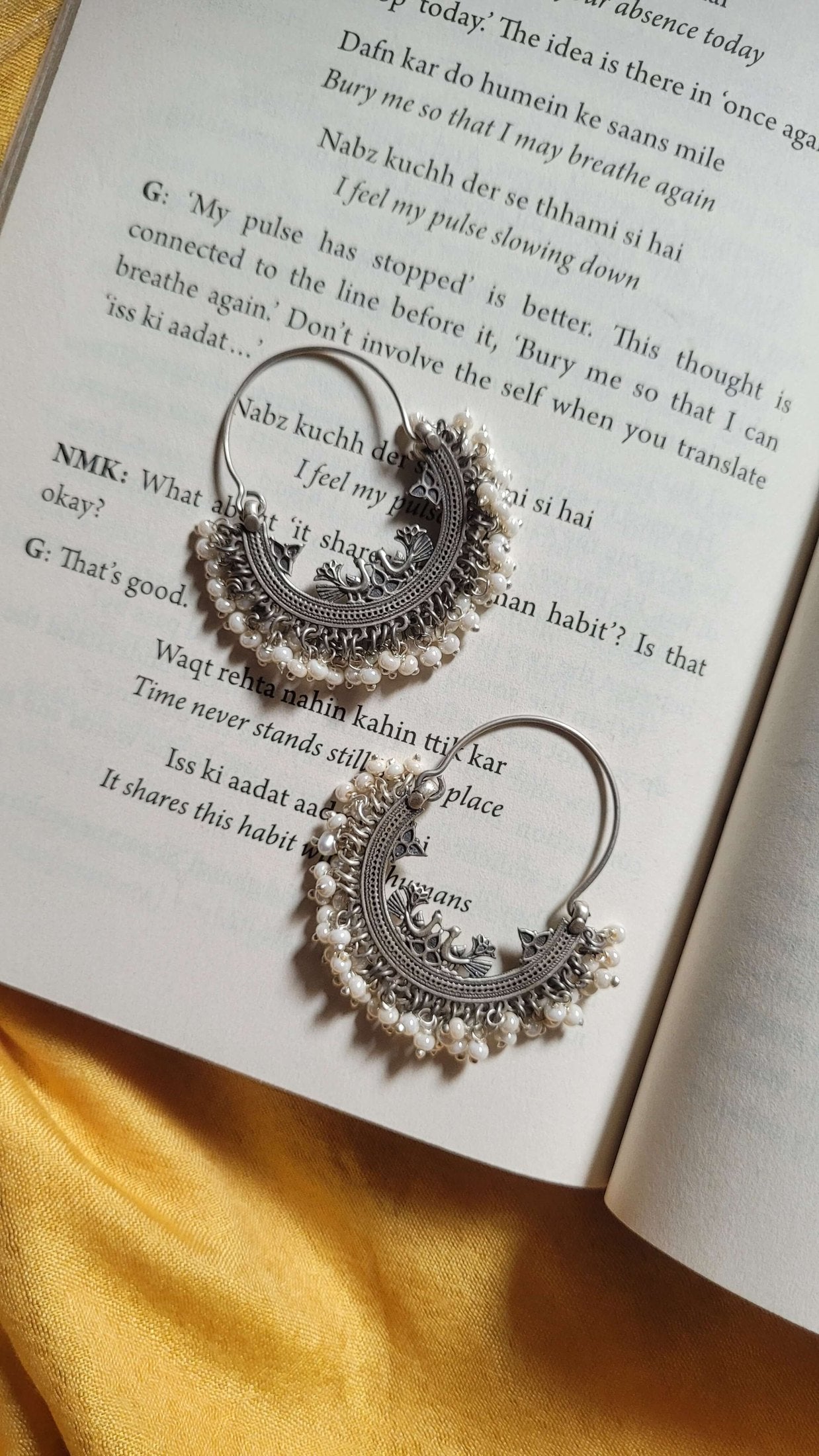 Decorative earrings on an open book with a yellow fabric background