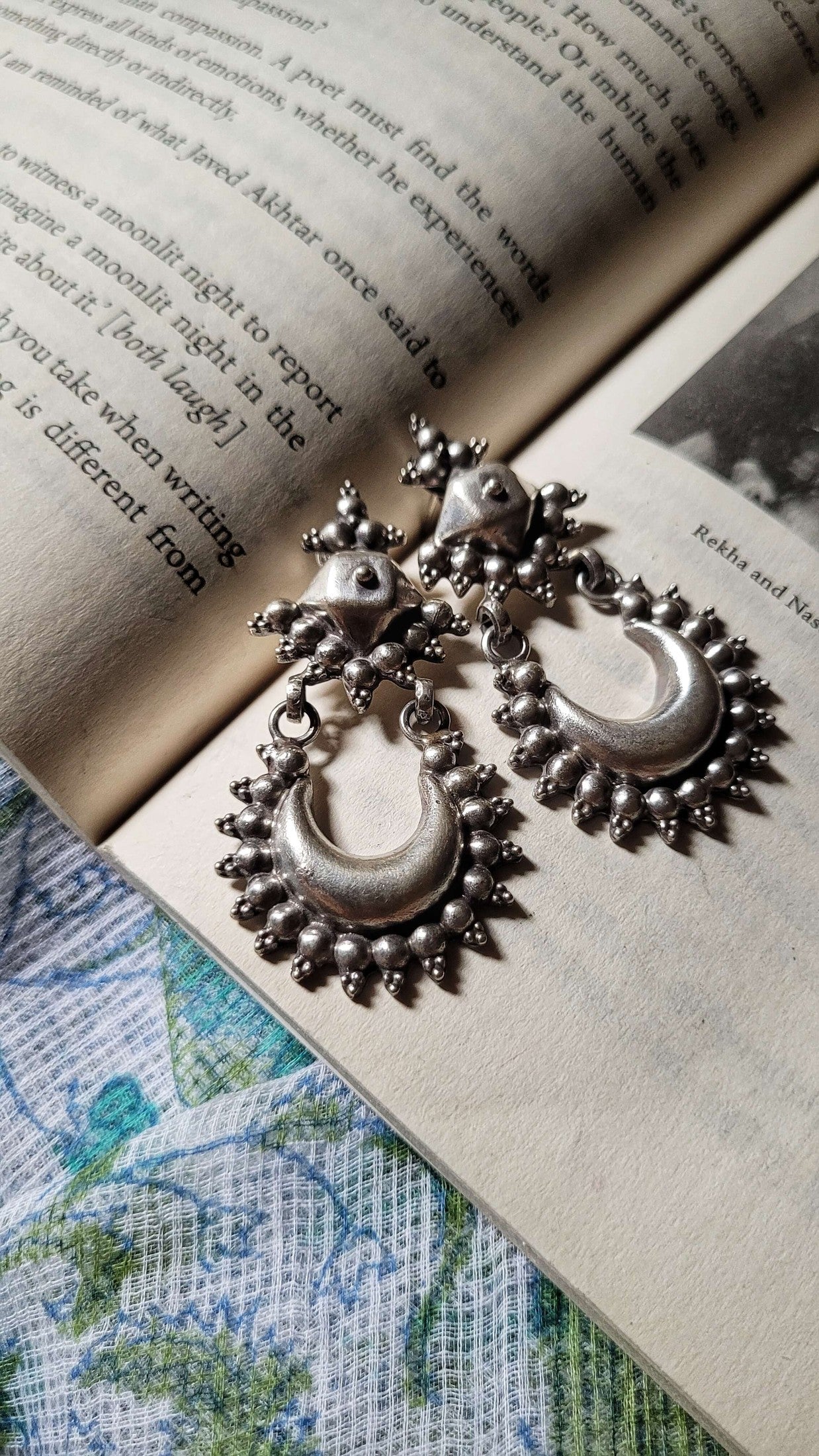 Ornate silver earrings on an open book with visible text and images.