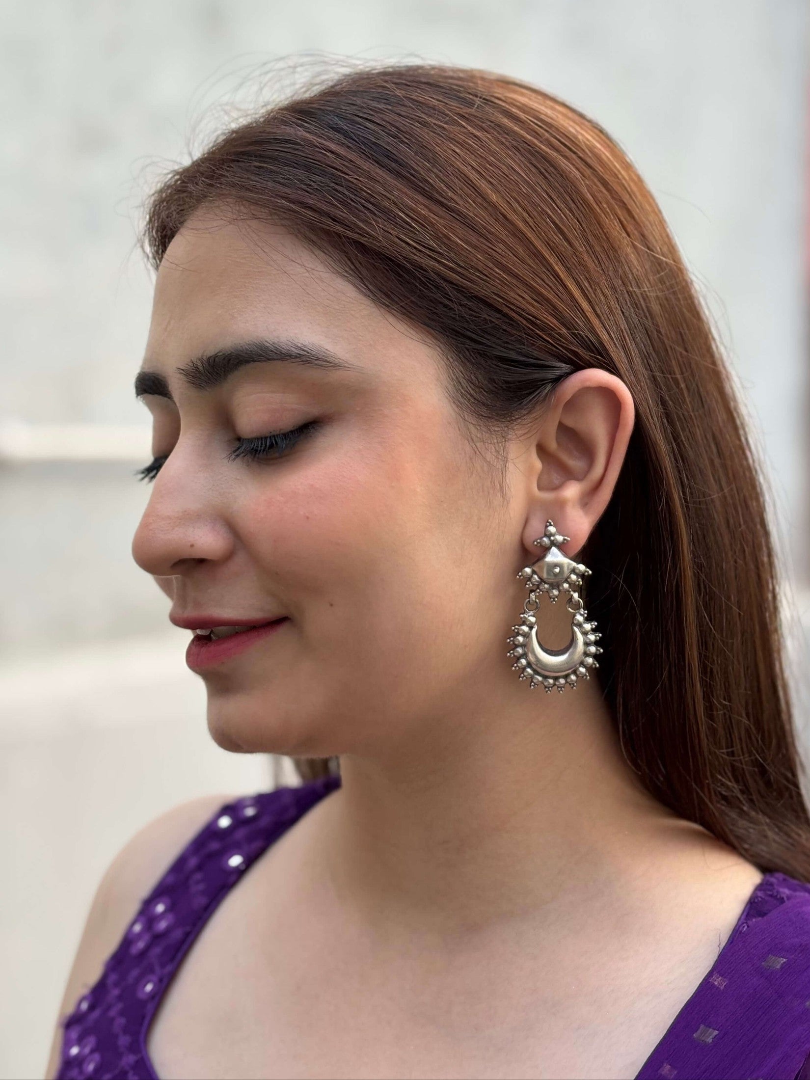 Woman wearing Nivetha Chandbaali and a purple top with hoop earrings against a blurred background