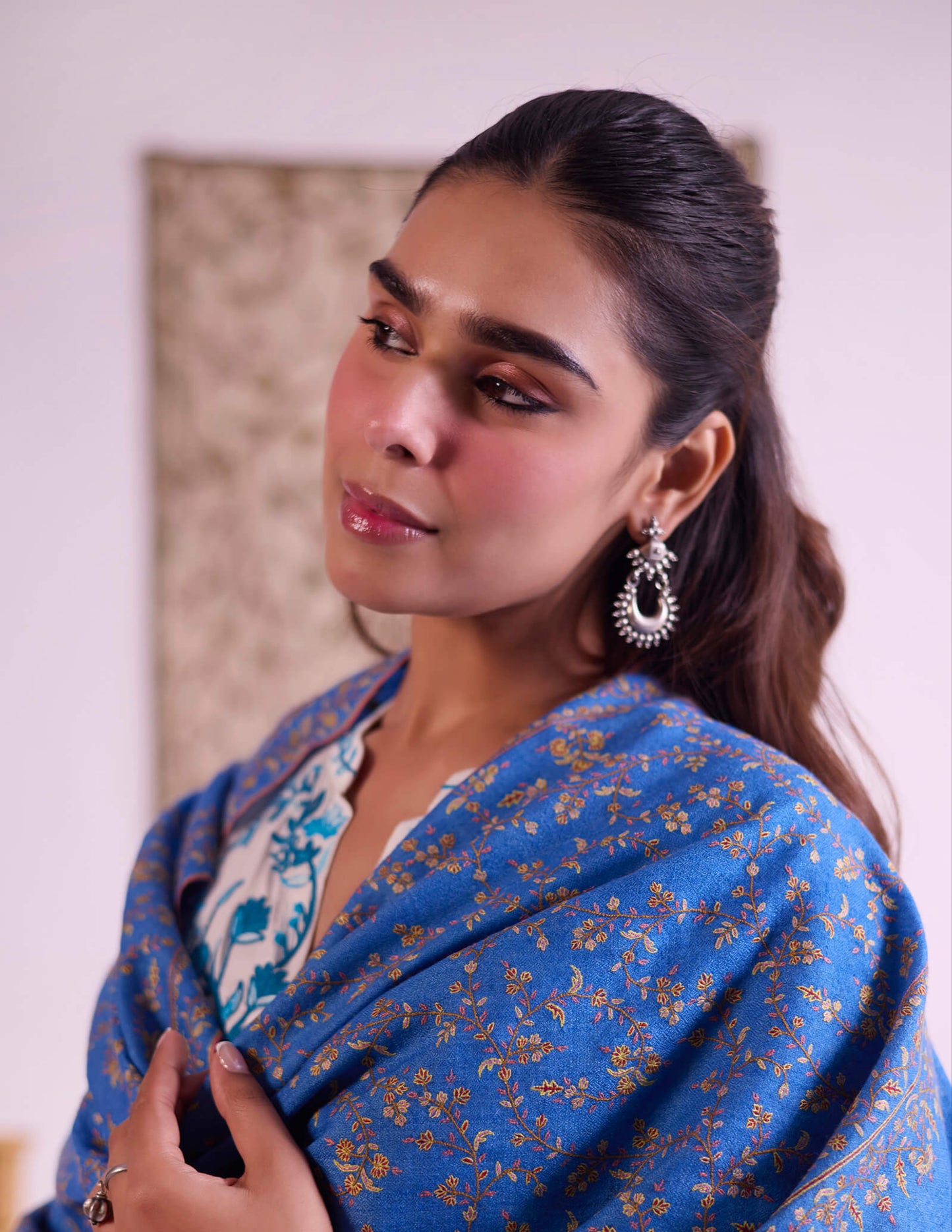 Woman wearing a blue saree with gold patterns, standing indoors.