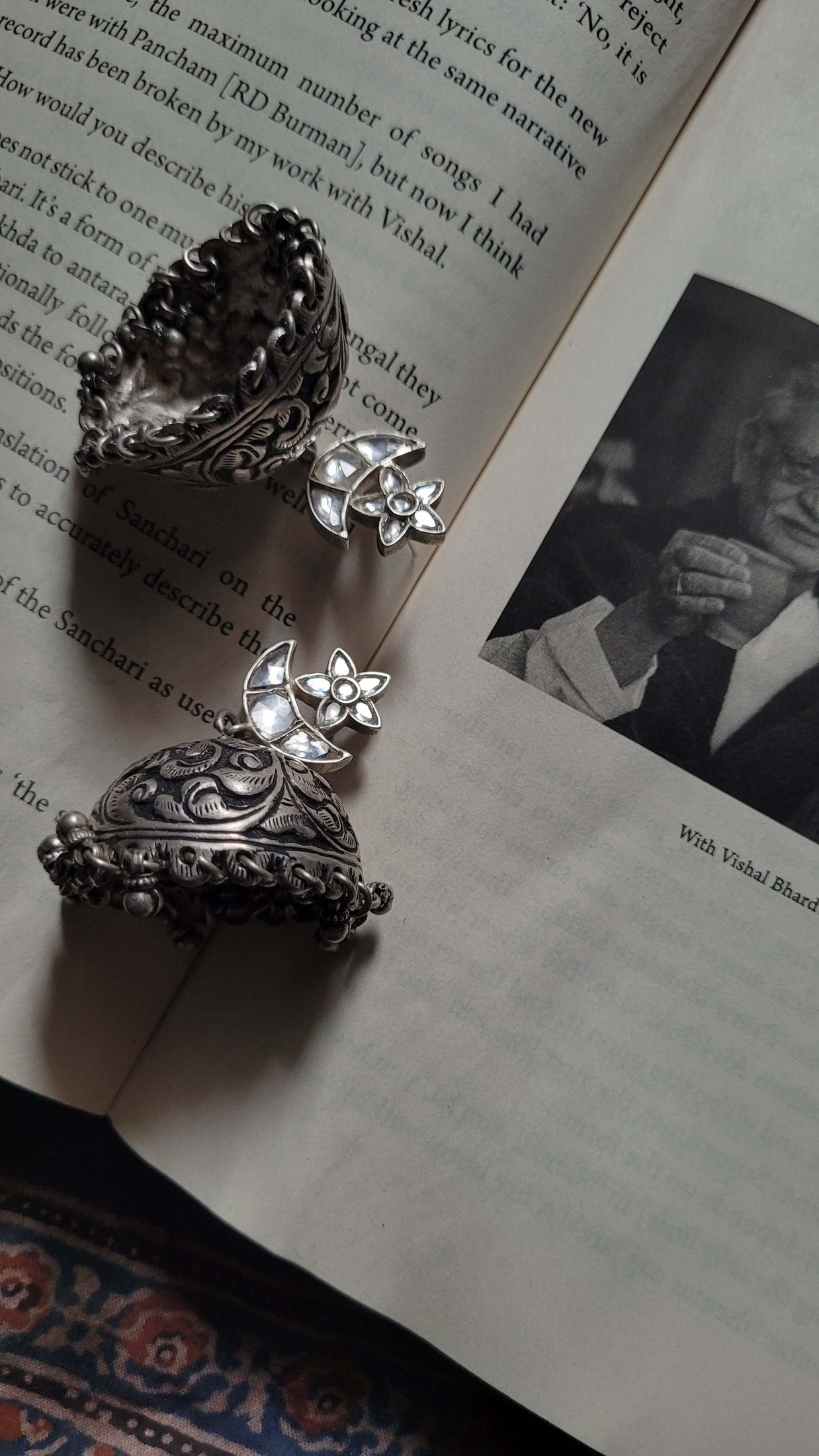 Silver earrings on an open book with a black and white photo of a person.