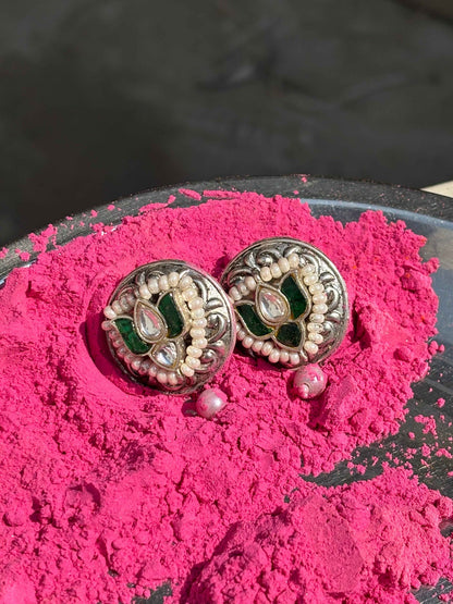 Decorative green kundan silver earrings on a pink powdery surface with a blurred background