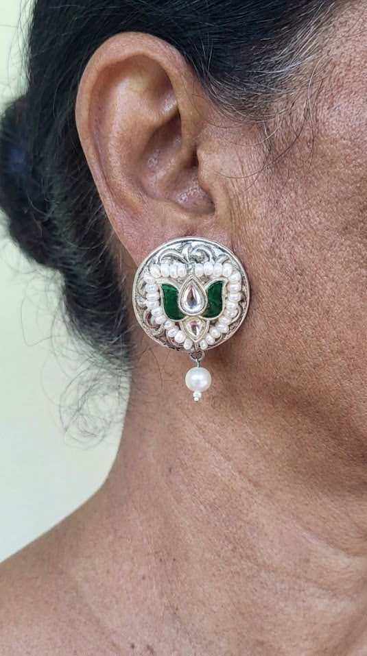 Close-up of an ear wearing a silver earring with green kundan and pearl.