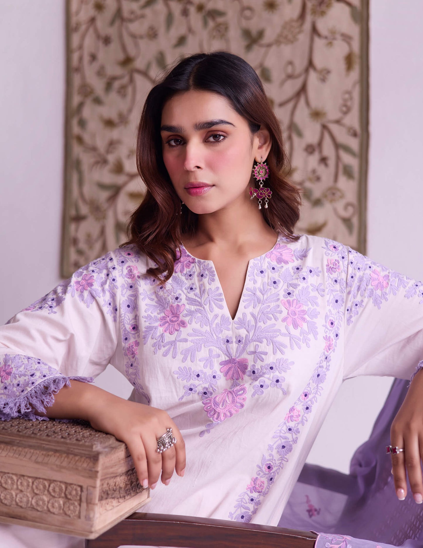 Woman in a floral outfit sitting on a chair with a decorative background