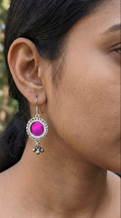 Close-up of an ear wearing a magenta pink glass earring with silver details.