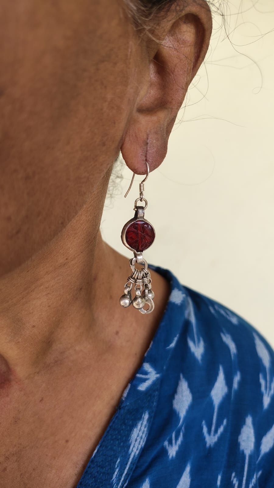 Close-up of an earring worn by a person with a blue patterned garment.