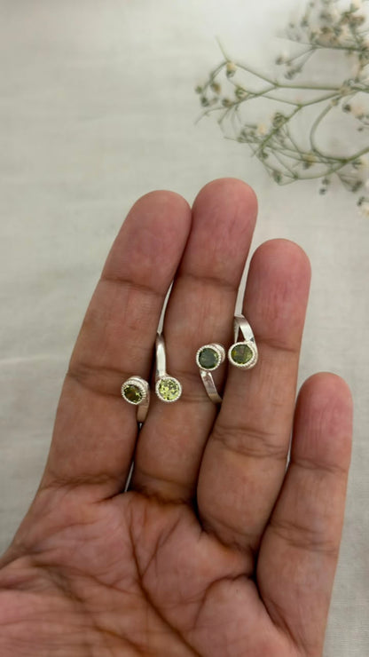 Two 92.5 silver rings with round green gemstones displayed on an open hand, with small dried flowers in the background.