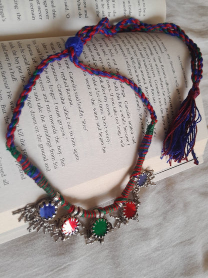 A colorful braided necklace with silver-toned star-shaped charms and blue, red, green, and white stones, laid on top of an open book.