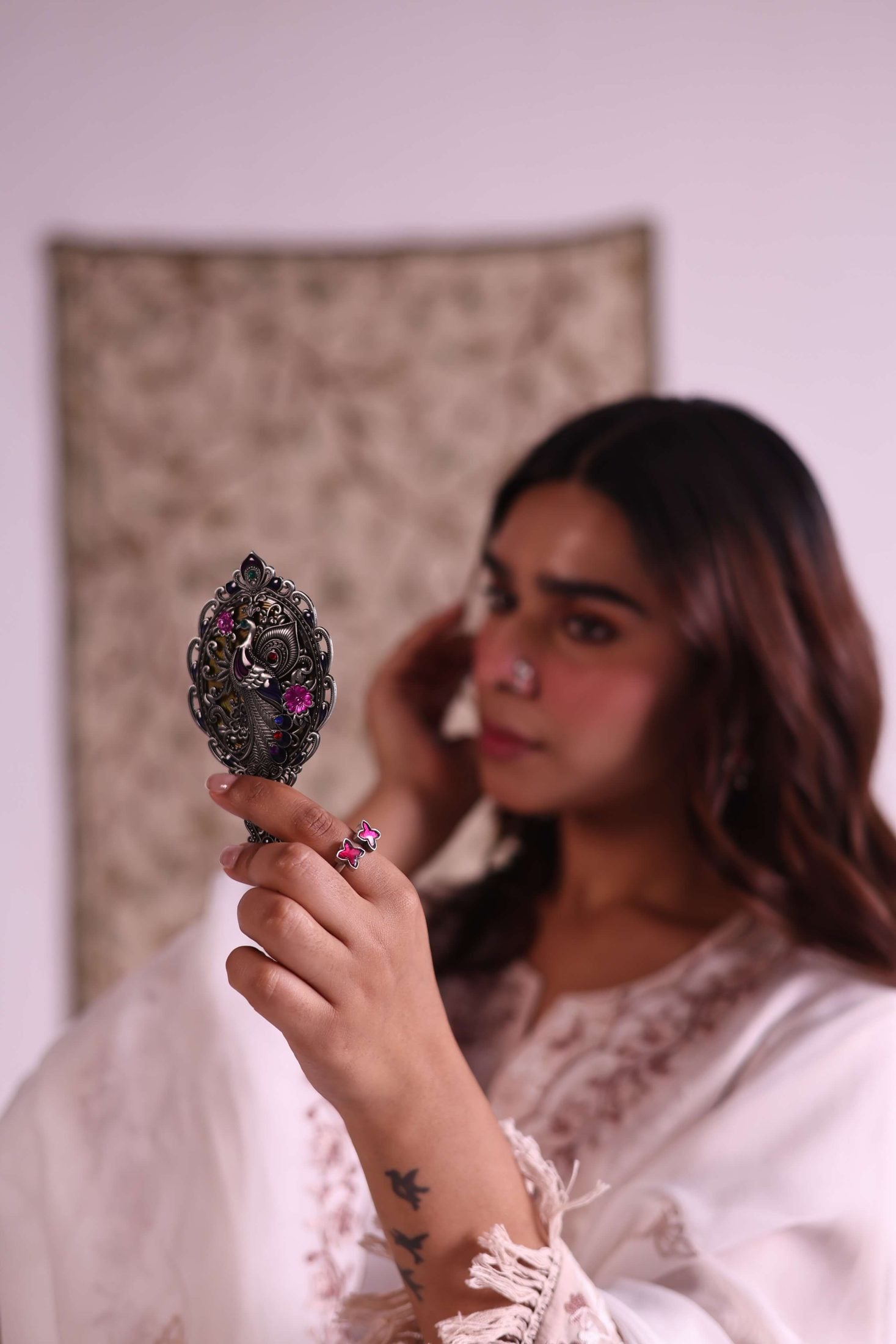 Woman holding a decorative mirror with intricate designs, wearing a white garment.
