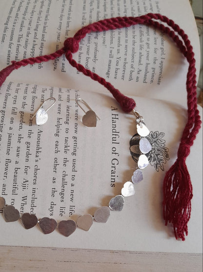 A handmade heart-shaped silver chain bracelet with a red braided cord and tassel, displayed on an open book.