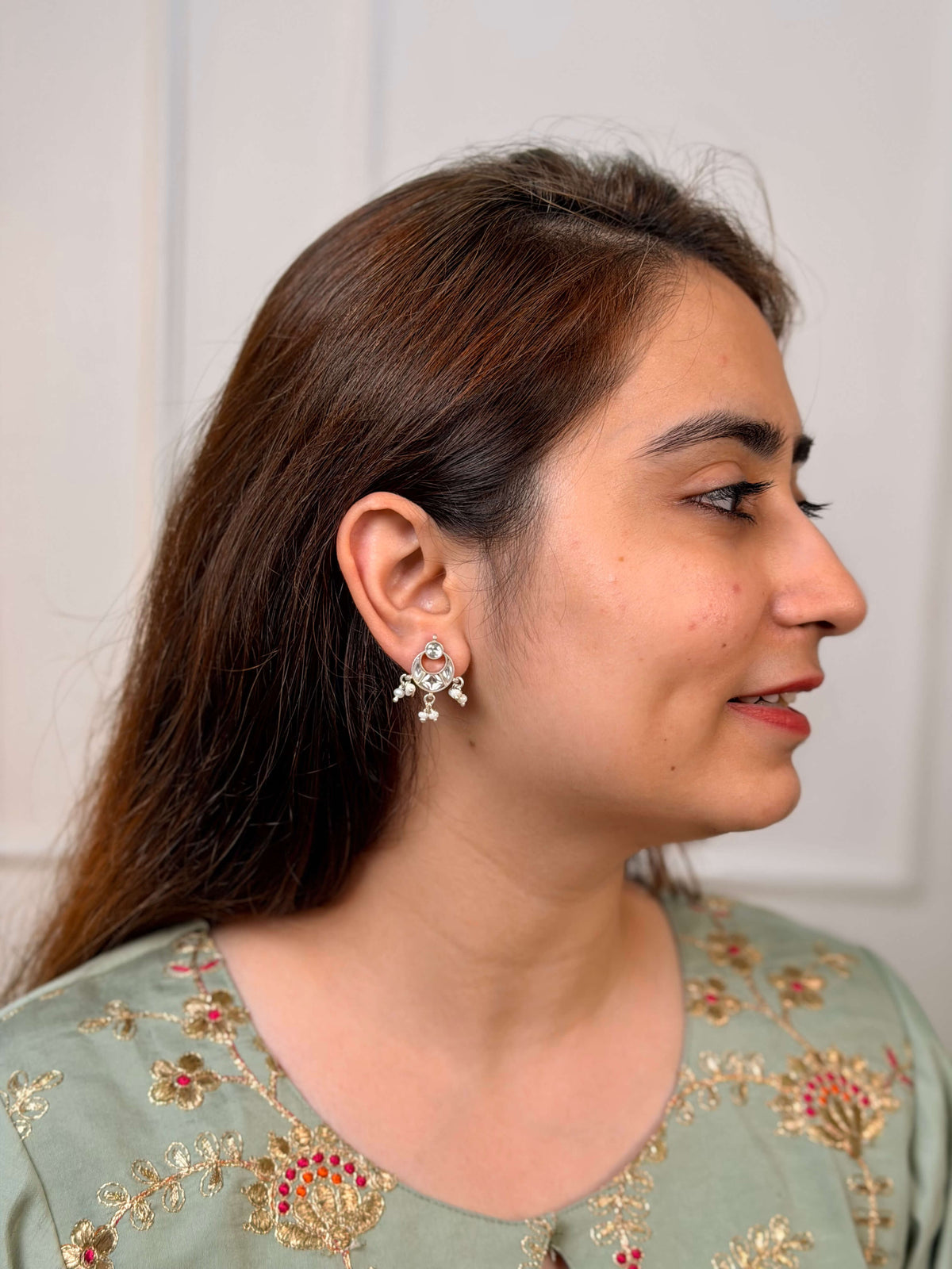 A close-up lifestyle shot of a woman wearing a silver-toned, kundan chandbali earrings with white stones and pearls.