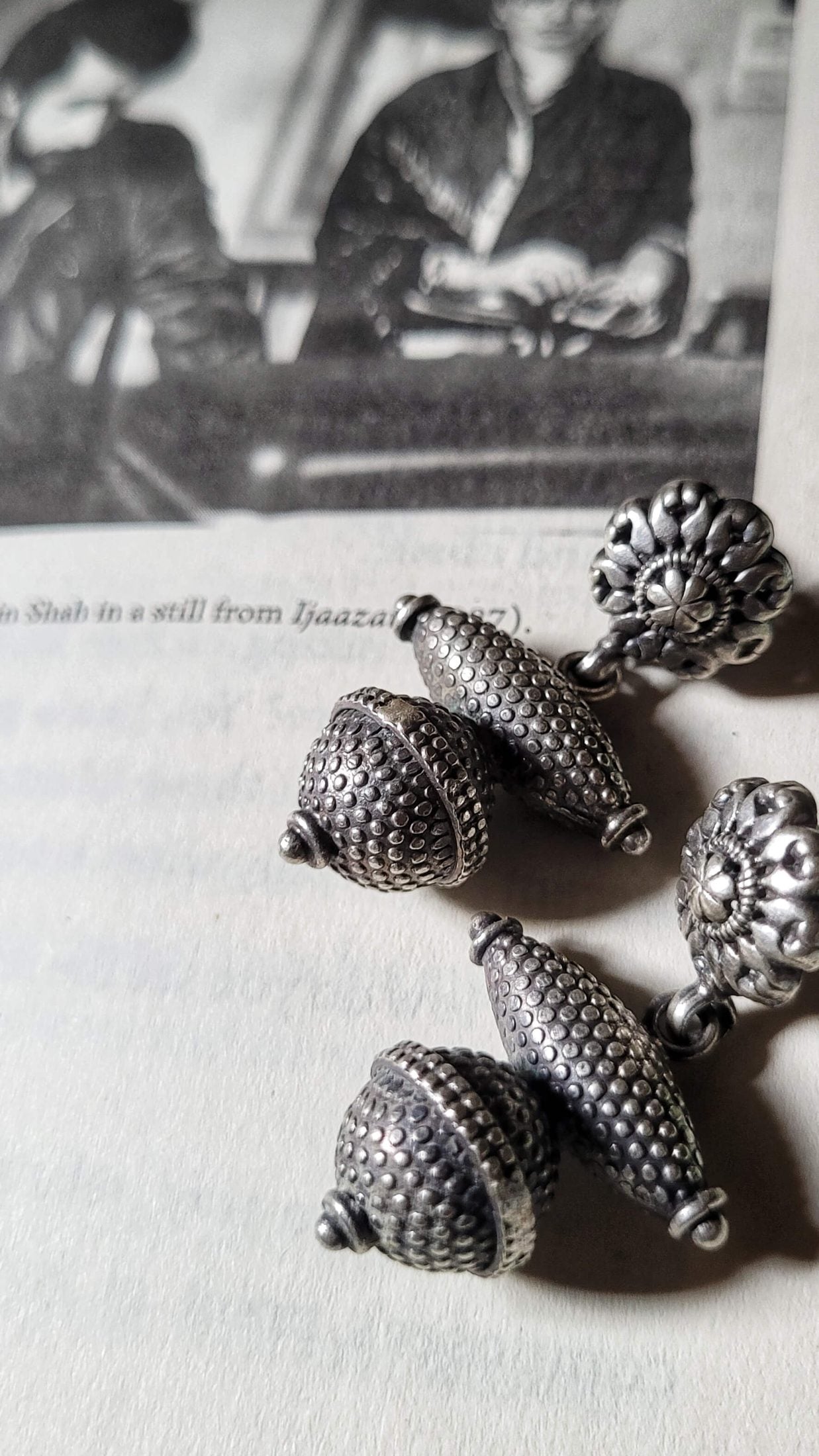 Silver acorn-shaped jewelry pieces on a textured surface with a blurred background