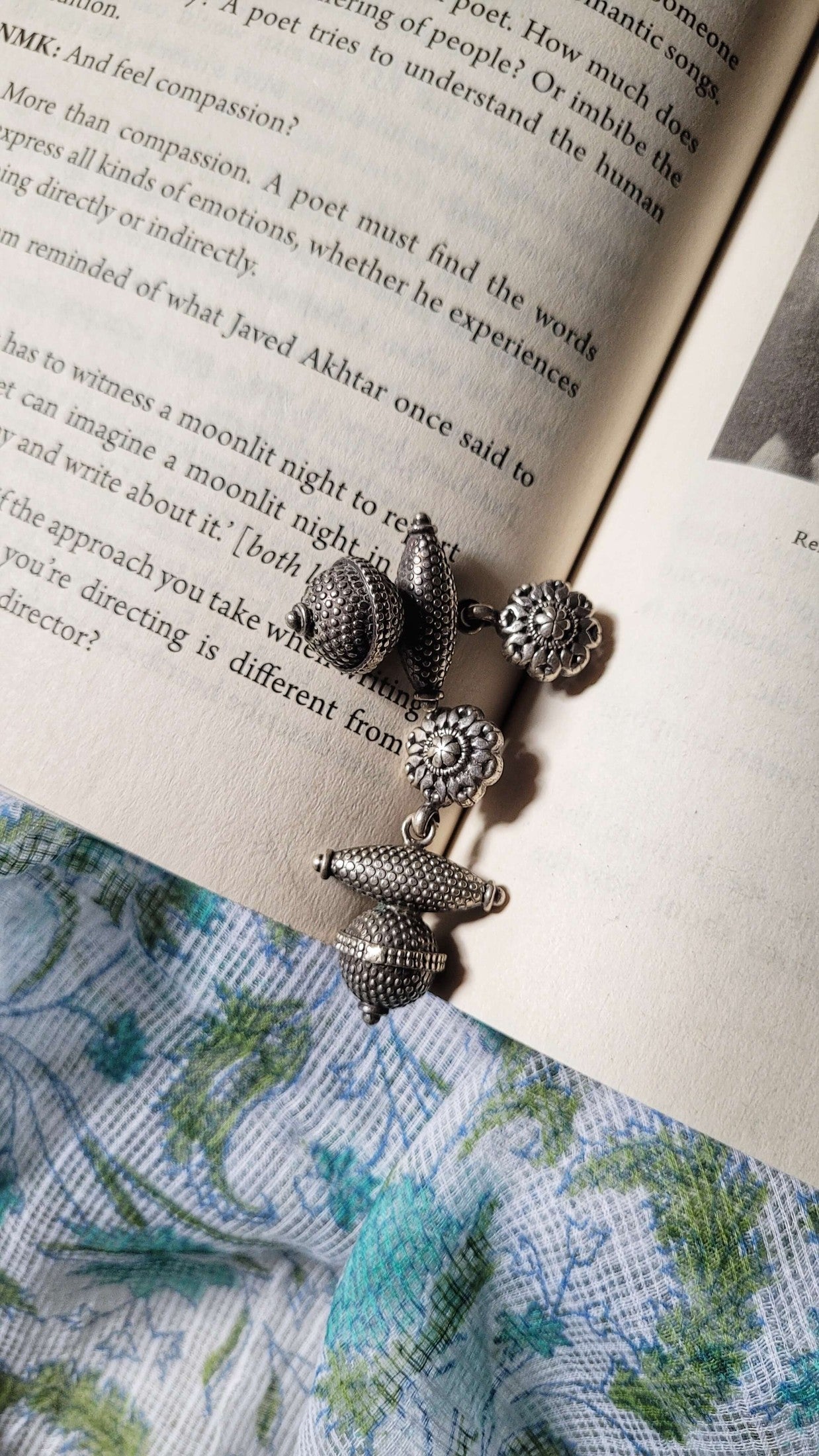 Silver earrings on an open book with floral fabric underneath