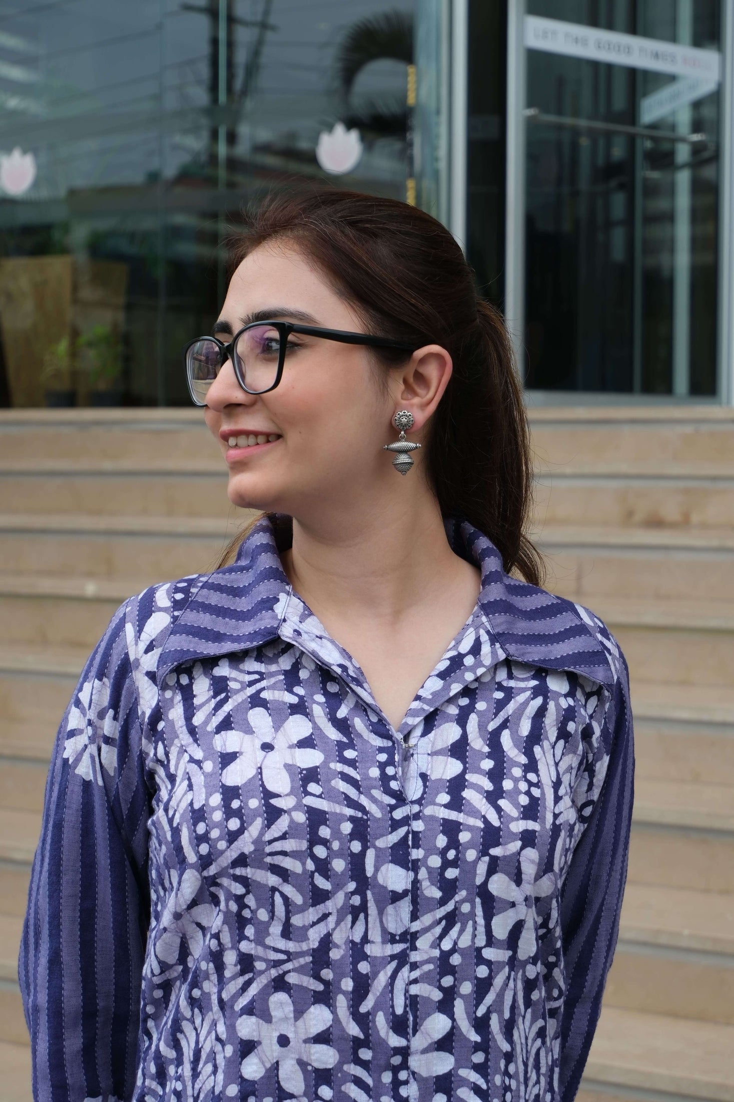 Person wearing a purple floral-patterned shirt with a blurred background and Riddhita Earrings.