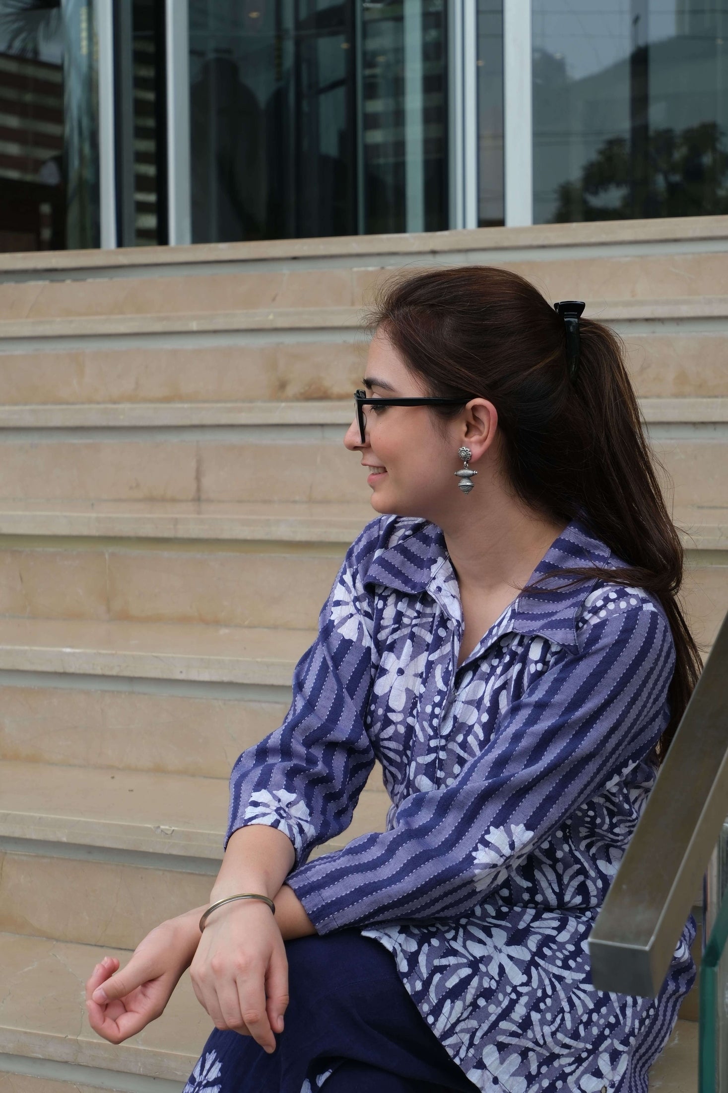 Woman in a blue and white patterned shirt standing outdoors with a building in the background and Riddhita Earrings.