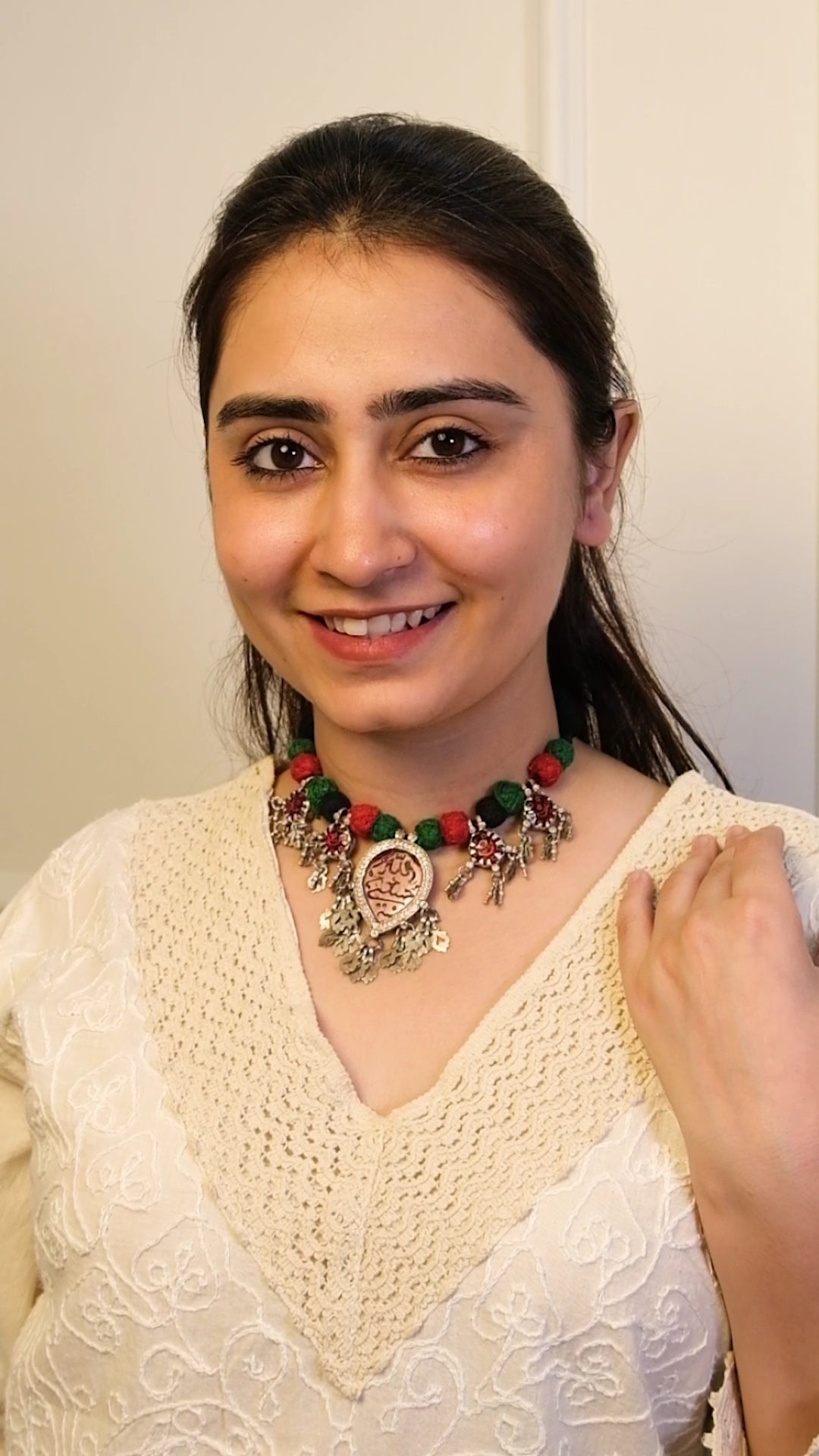 Woman wearing a white top and colorful necklace with a plain background