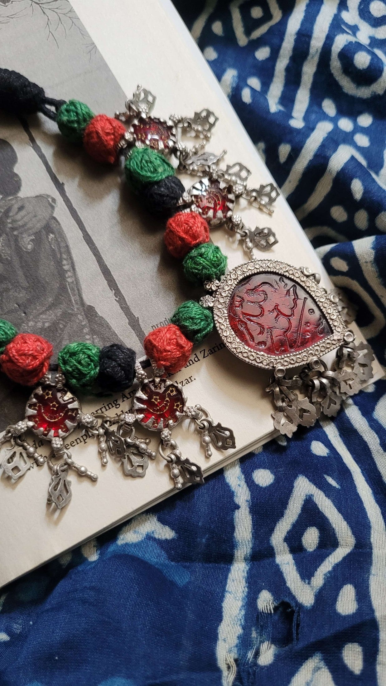 Vintage necklace with red glass stones, and green and black beads on a blue patterned fabric background
