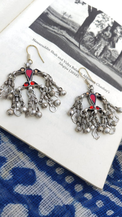 Pair of silver chandelier earrings with red accents on a blue and white patterned fabric.