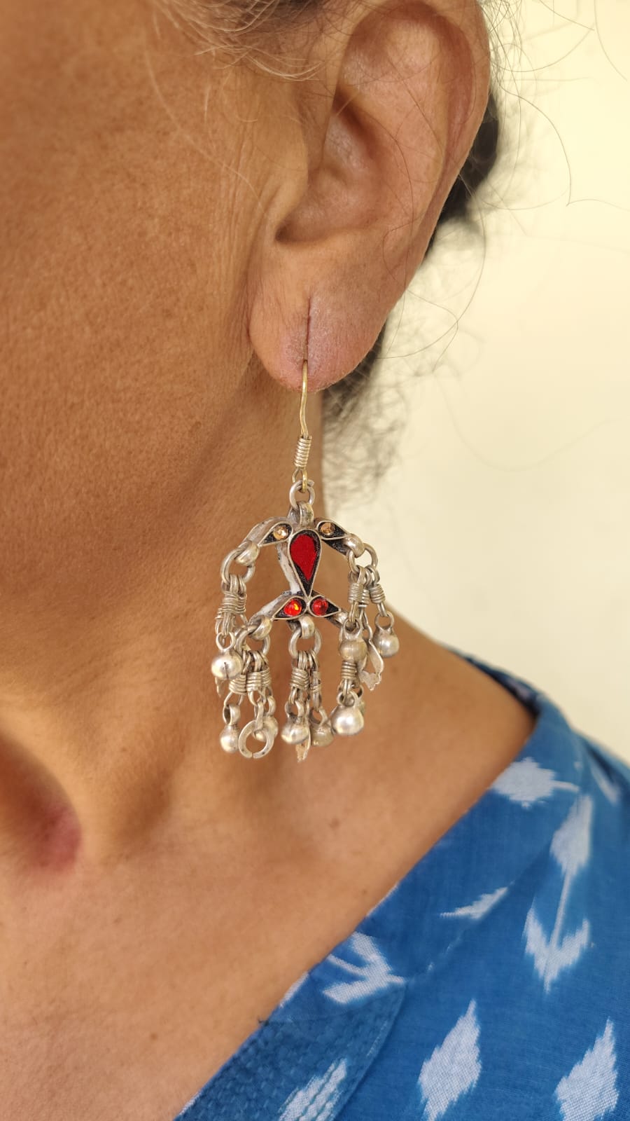 Close-up of a person wearing a silver earring with red glass stone and pearl-like silver beads.