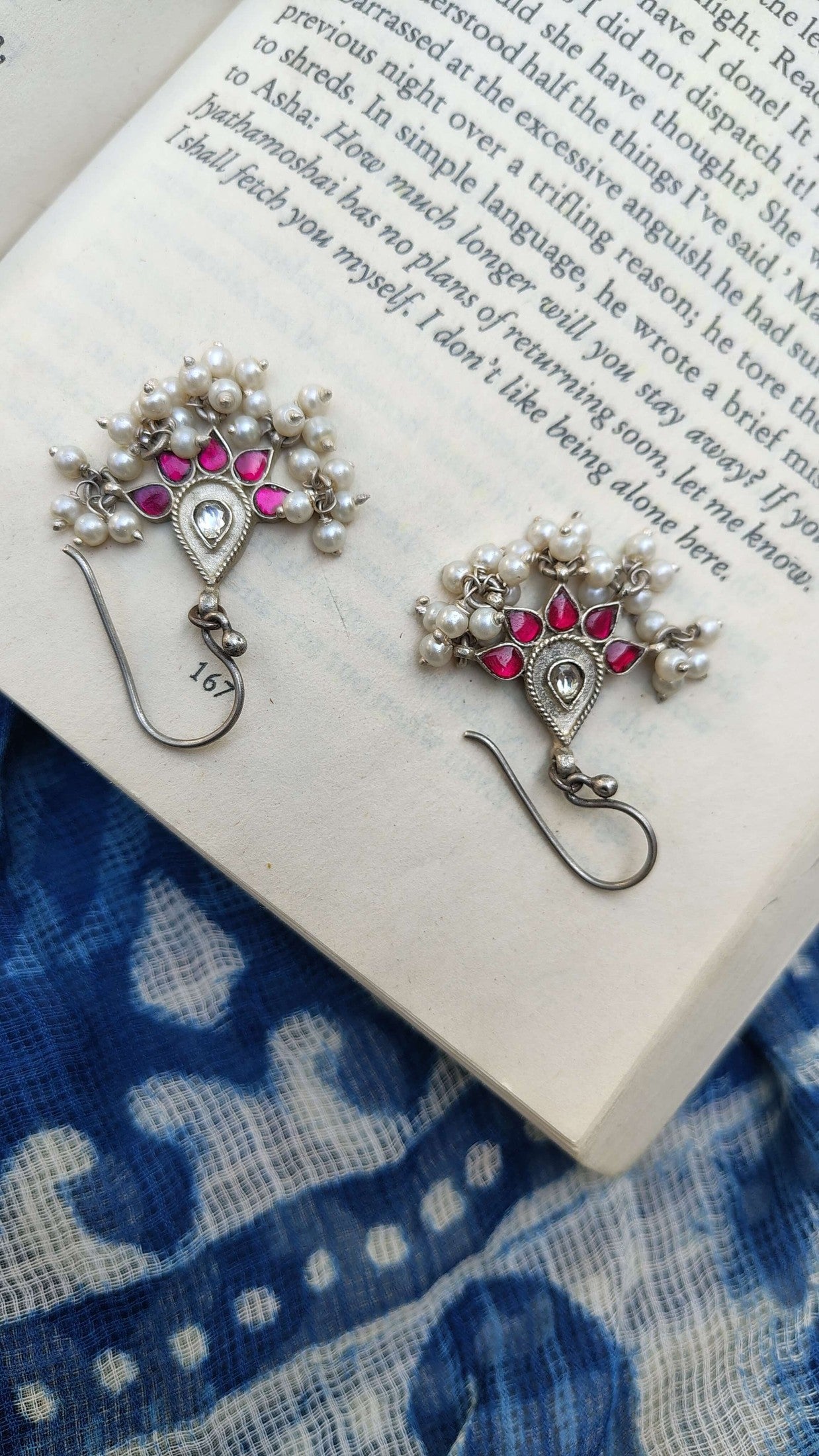 Pair of silver earrings with pink kundan stones and pearls on a book | Sadabahaar Jewelry