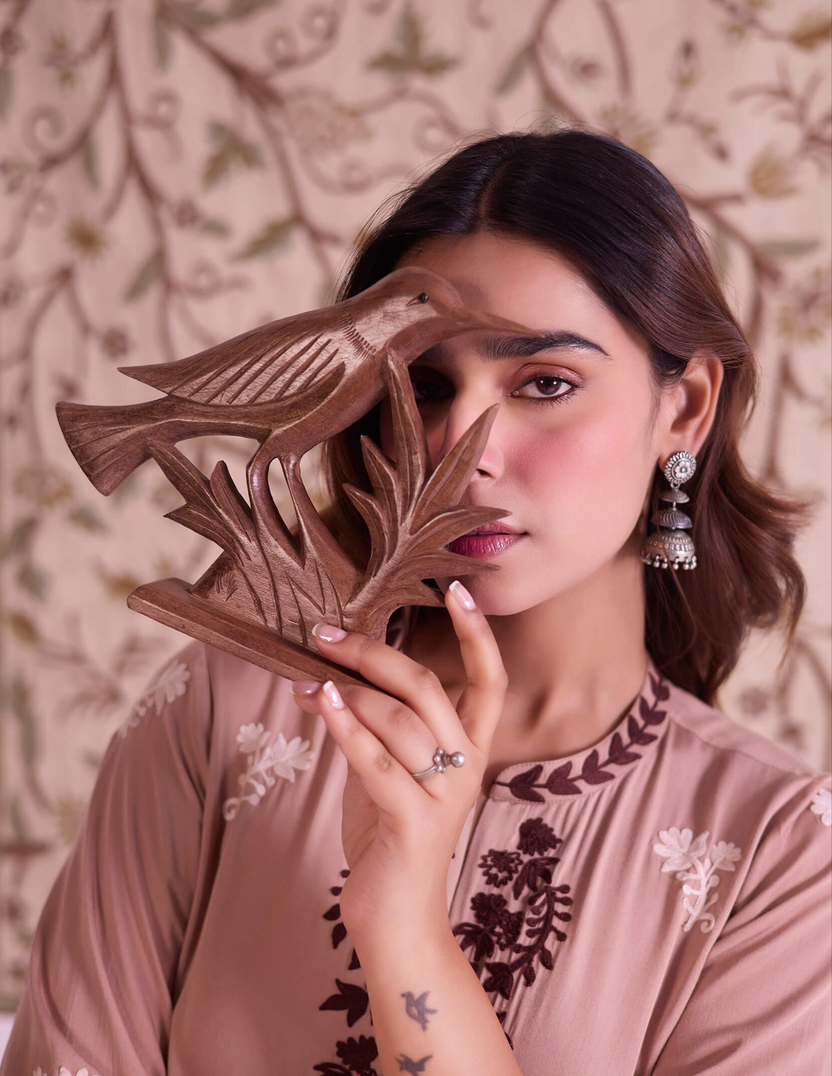 Woman holding a wooden sculpture against her face with a decorative background