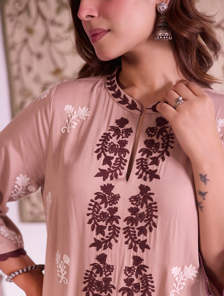 Woman wearing a light pink embroidered top with floral patterns.