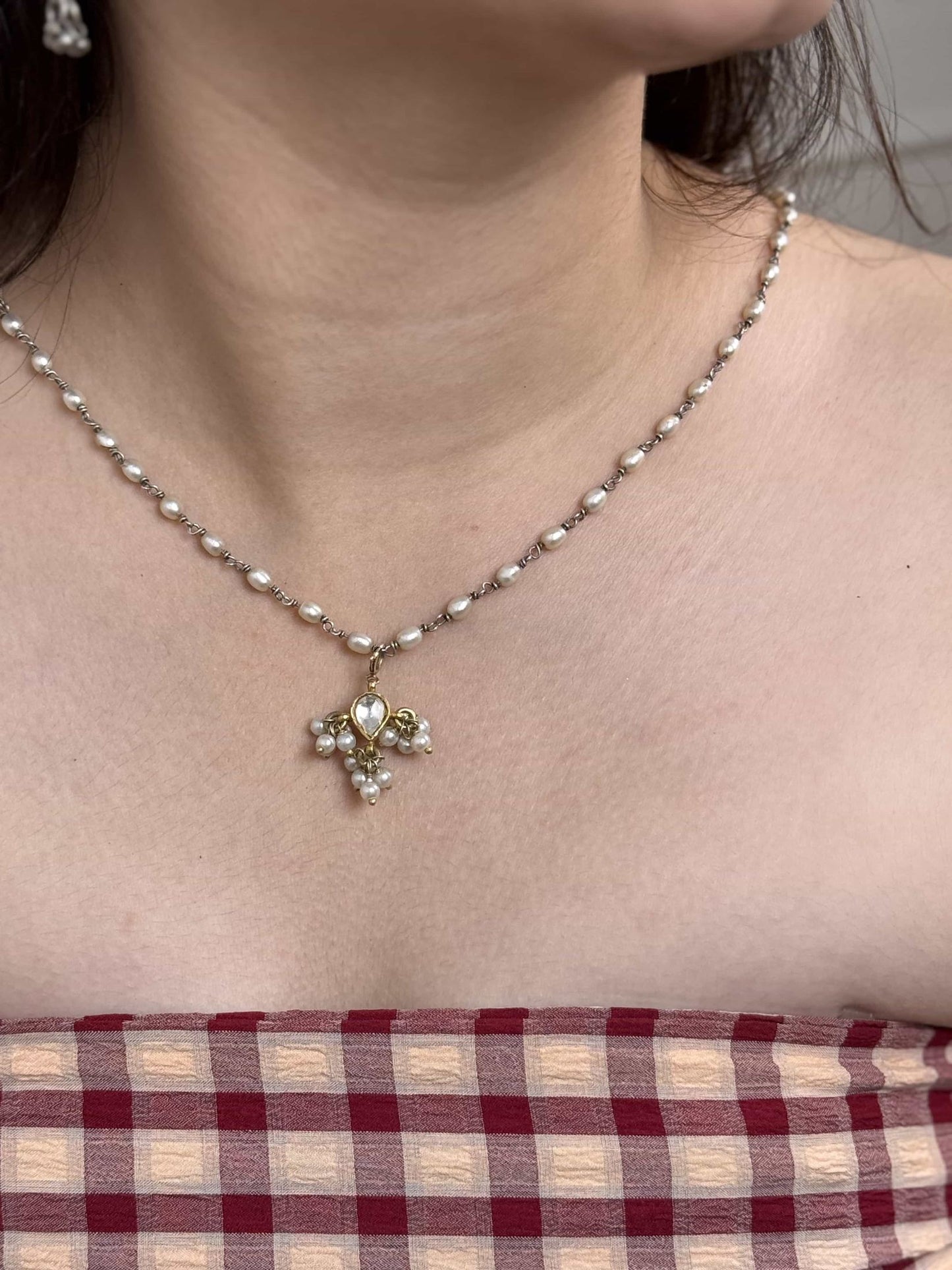 Necklace with a gold plated silver kundan pendant worn by a person, with a checkered fabric background.
