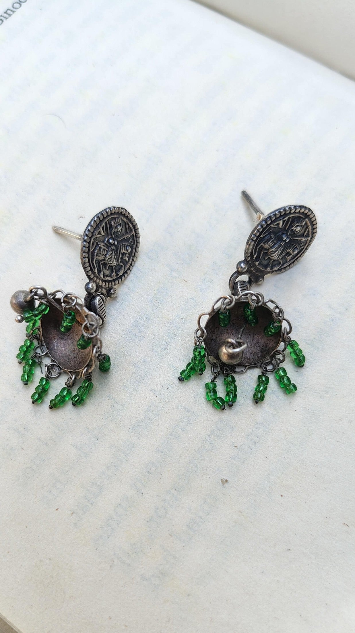 Pair of silver earrings with green gemstones on a white surface