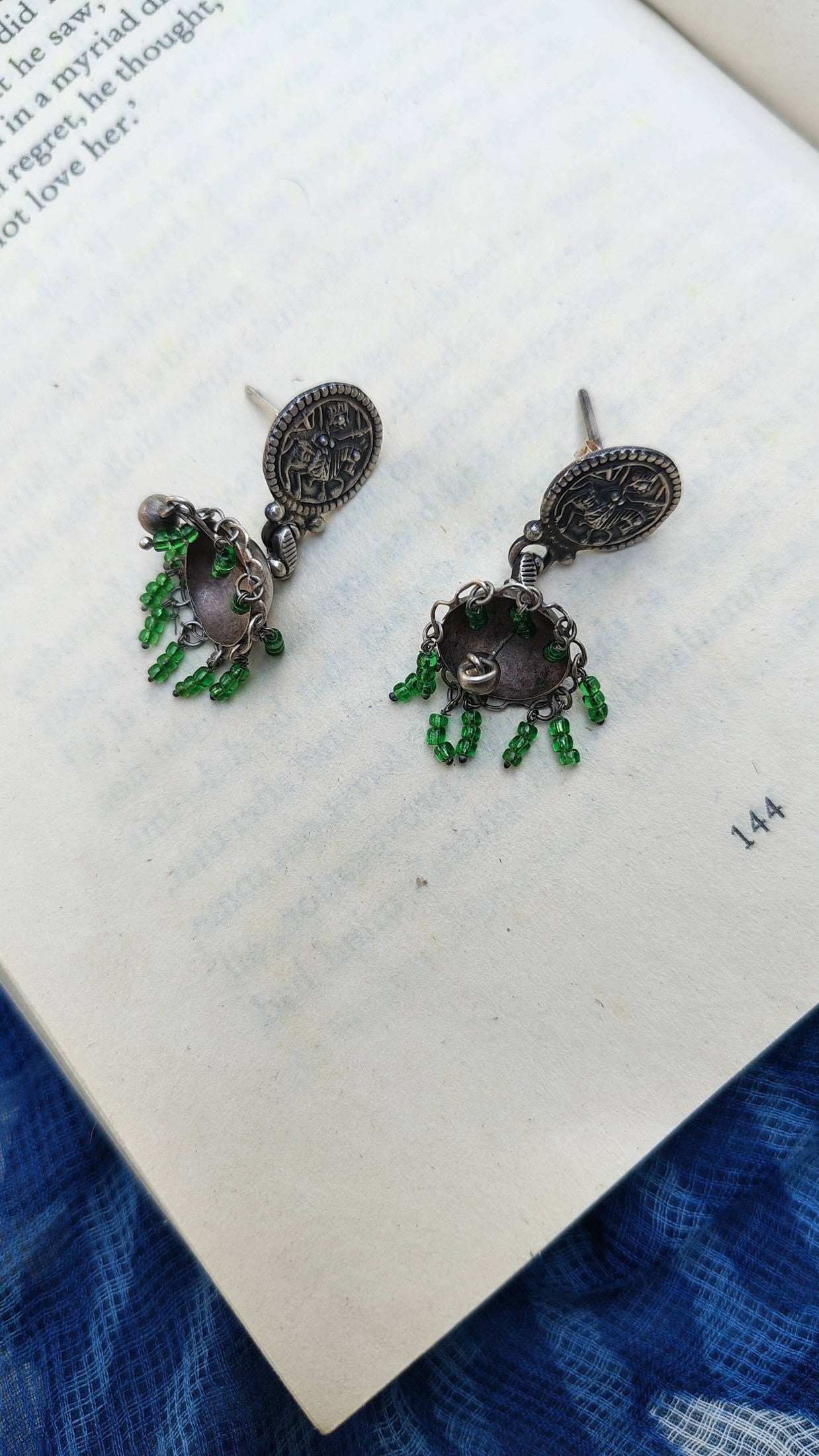 Pair of ornate earrings with green beads on a book page