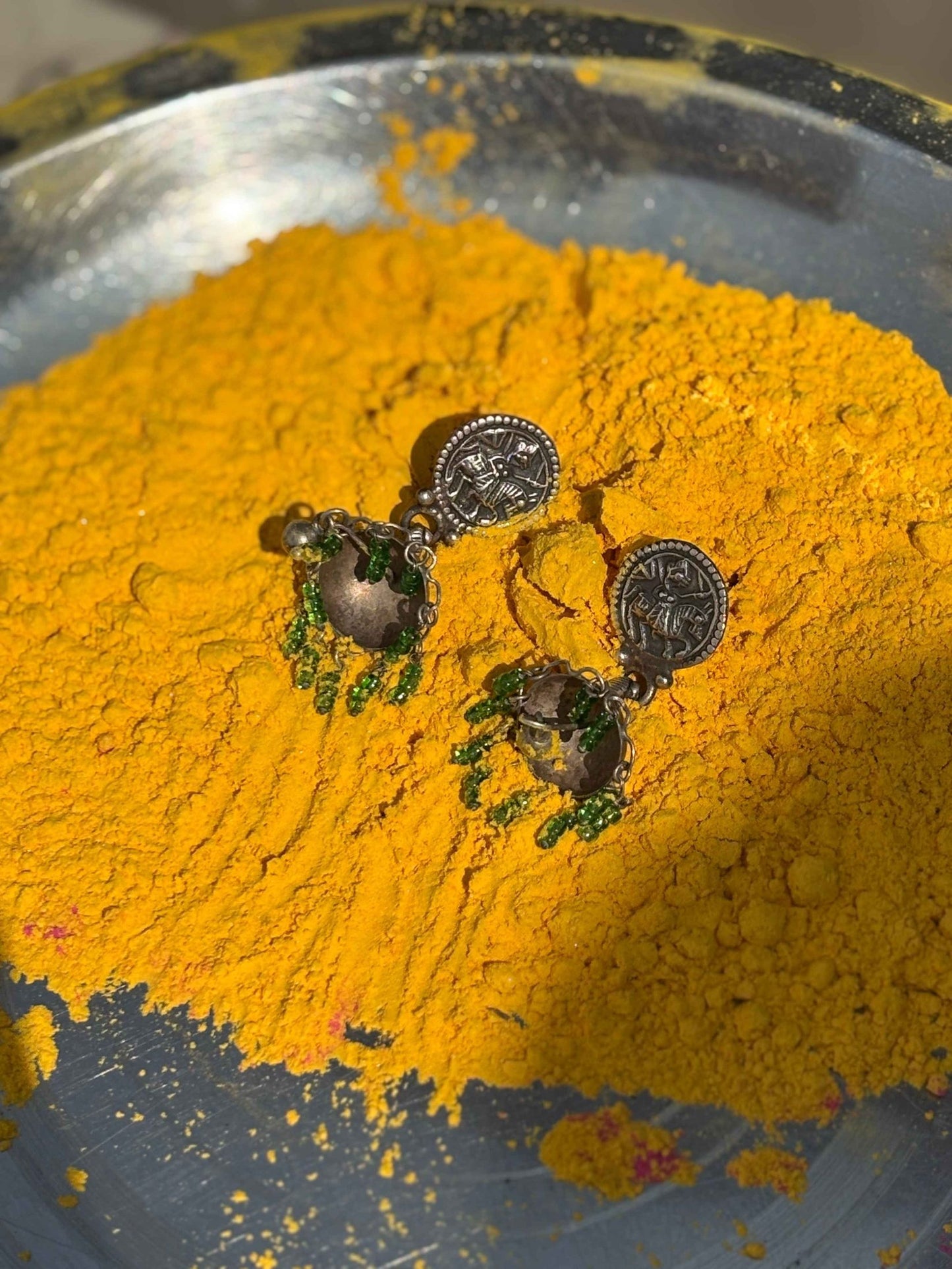 Pair of earrings on a bed of yellow powder in a metallic bowl