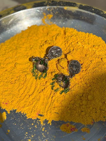 Pair of earrings on a bed of yellow powder in a metallic bowl