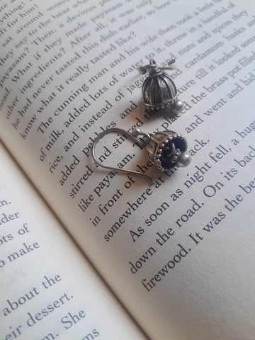 A pair of silver-toned jhumka earrings with decorative cabochon and floral details, displayed on the pages of an open book.