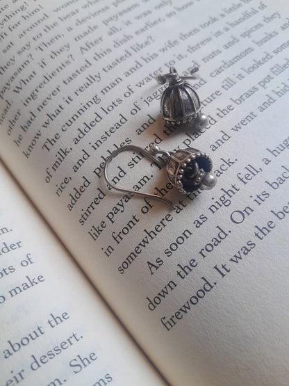 A pair of silver-toned jhumka earrings with decorative cabochon and floral details, displayed on the pages of an open book.