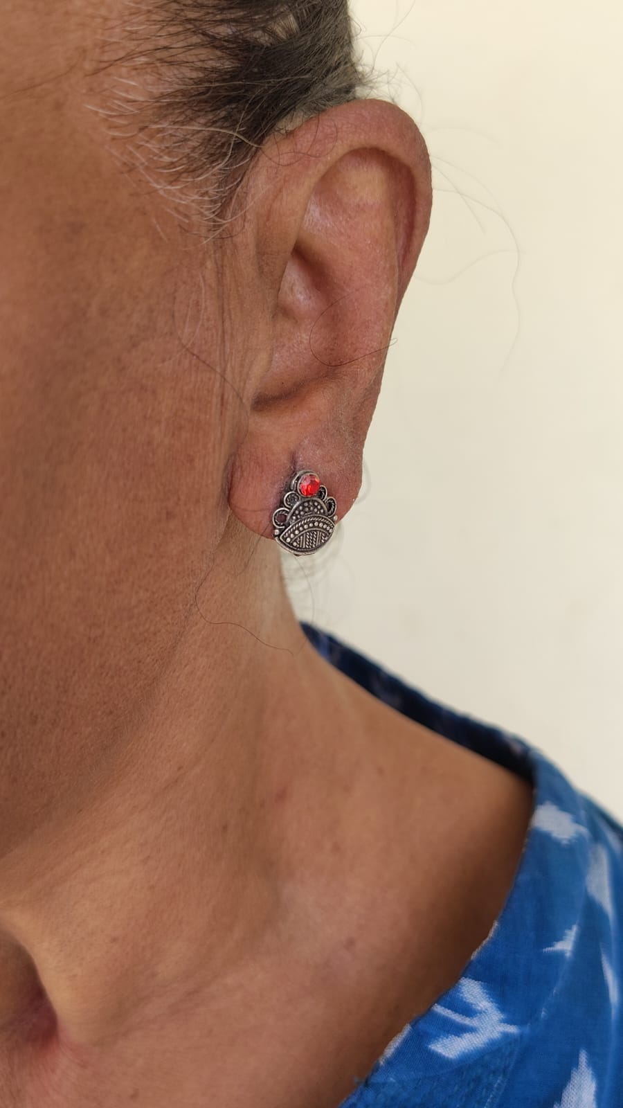 Close-up of an ear wearing a small earring with a red gemstone on a plain background